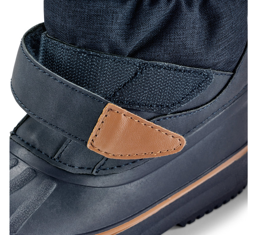 Gros plan sur une botte polyvalente pour enfant, botte bleue avec fermeture velcro et détail en cuir marron.