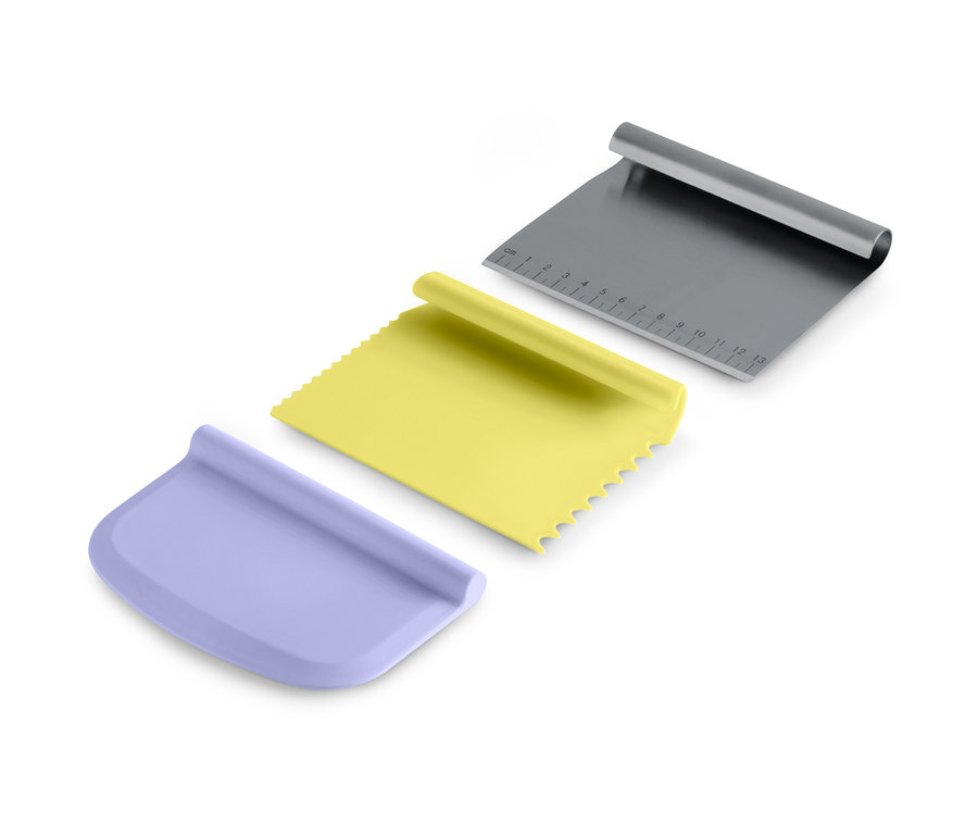 Lot d'ustensiles de pâtisserie : un grattoir violet, un grattoir jaune dentelé et un grattoir en métal avec une échelle de mesure.