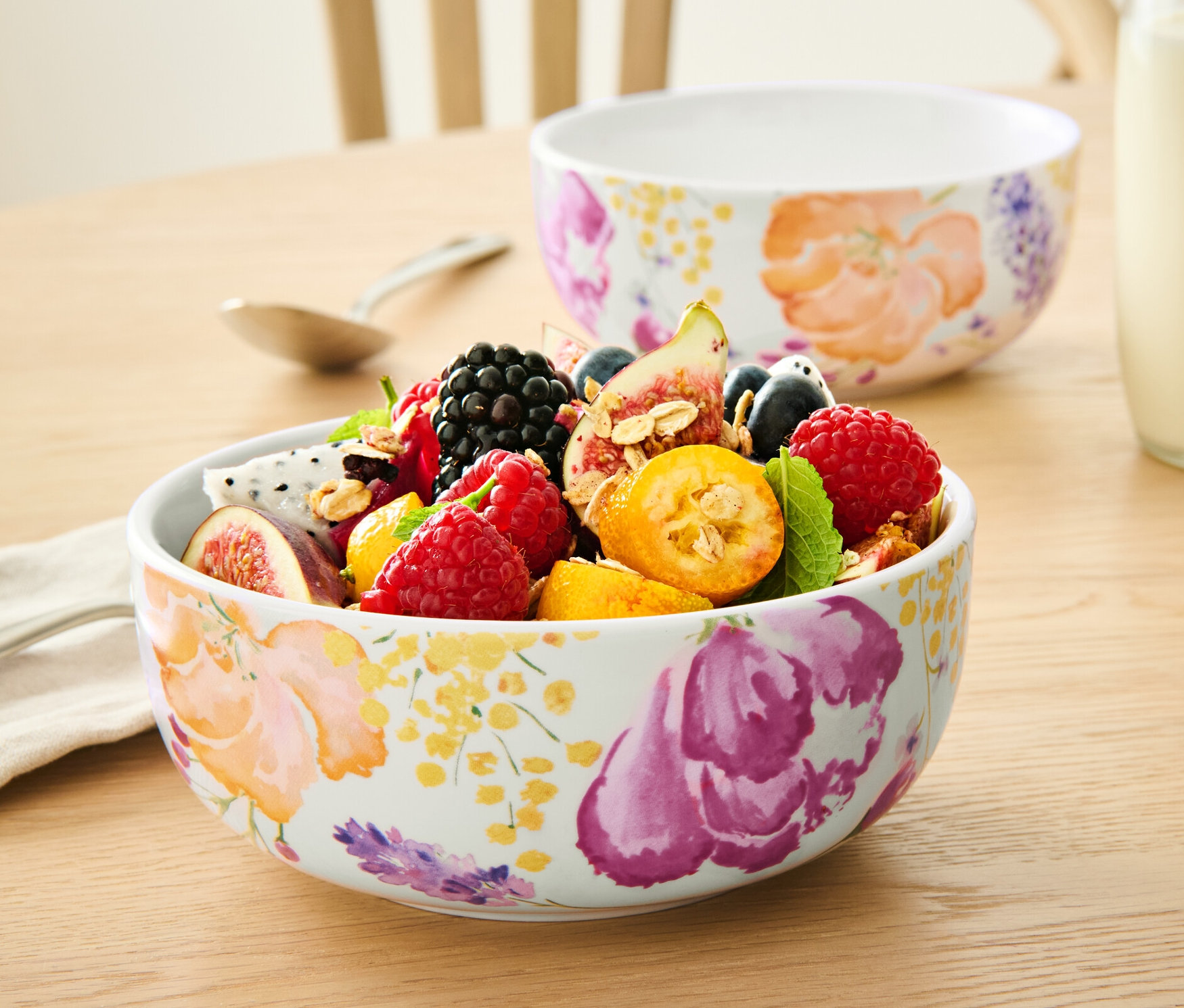 Sur une table, deux 2 bols remplis de fruits, une bouteille de lait et une tasse de liquide.