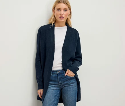 Une femme blonde porte un cardigan long ouvert, un t-shirt blanc et un jean.