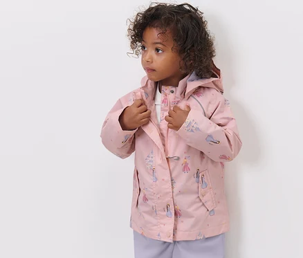 Une fille ferme sa veste de pluie pour enfant avec un imprimé de princesses.
