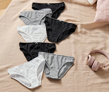 Sept culottes pour enfant, blanches, grises et noires, sont posées sur un lit à côté d'un casque rose.
