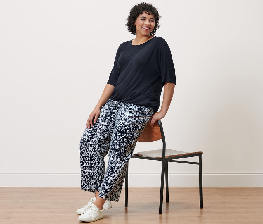 Une femme est assise sur une chaise et porte une blouse bleu foncé et un pantalon tissé à imprimé intégral.