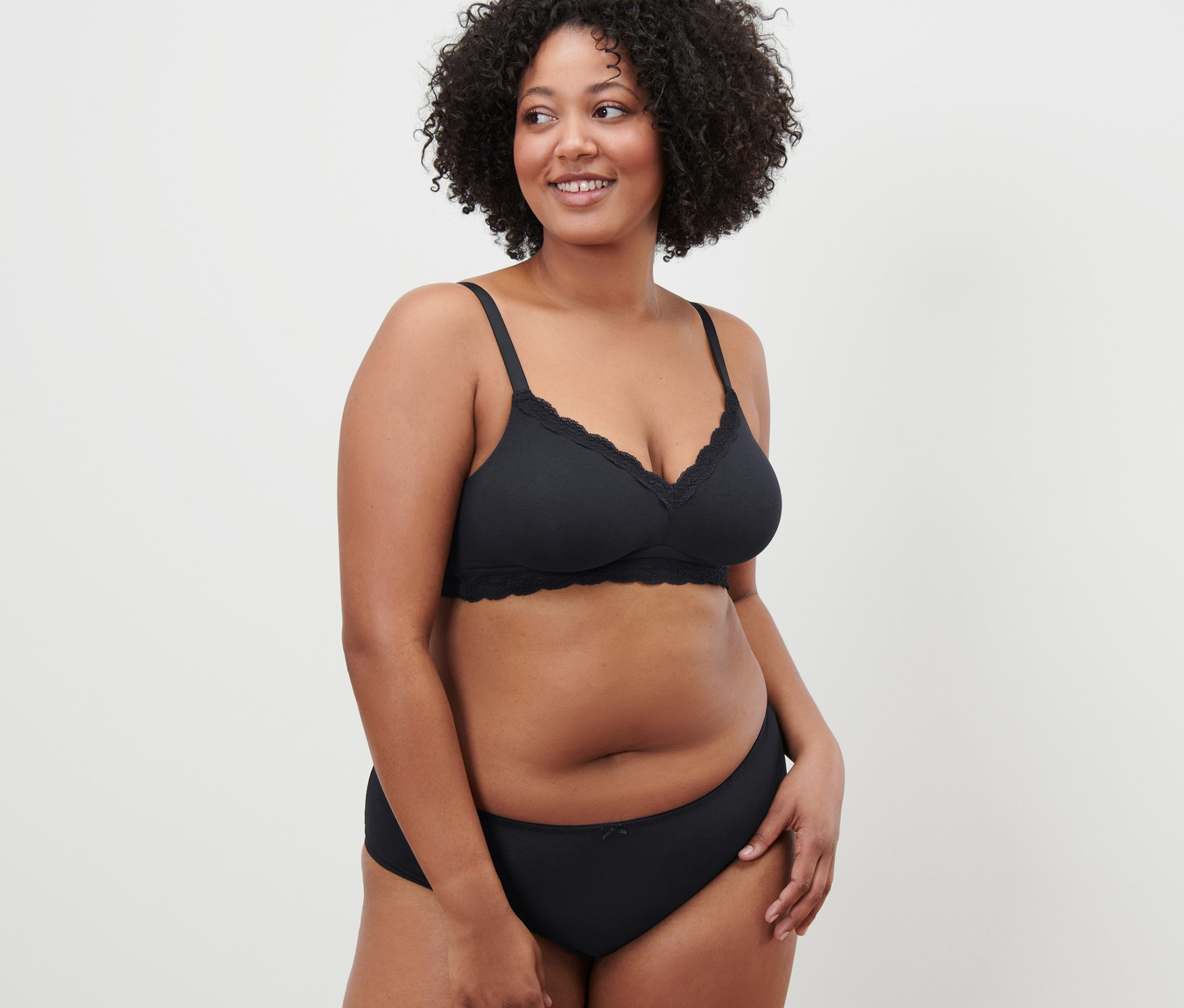 Femme aux cheveux bouclés posant en soutien-gorge souple noir.