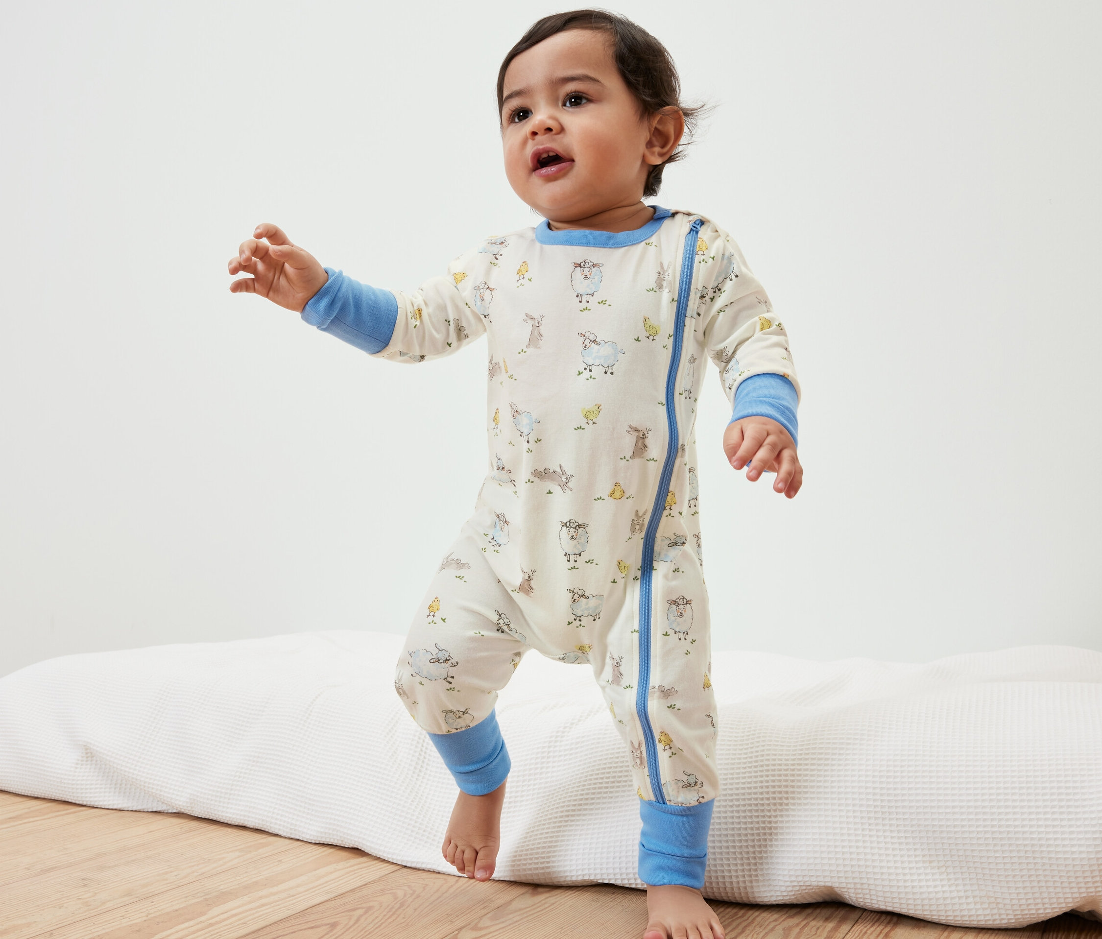 Bambin debout sur un tapis, vêtu d'un pyjama pour bébé avec des motifs d'animaux.