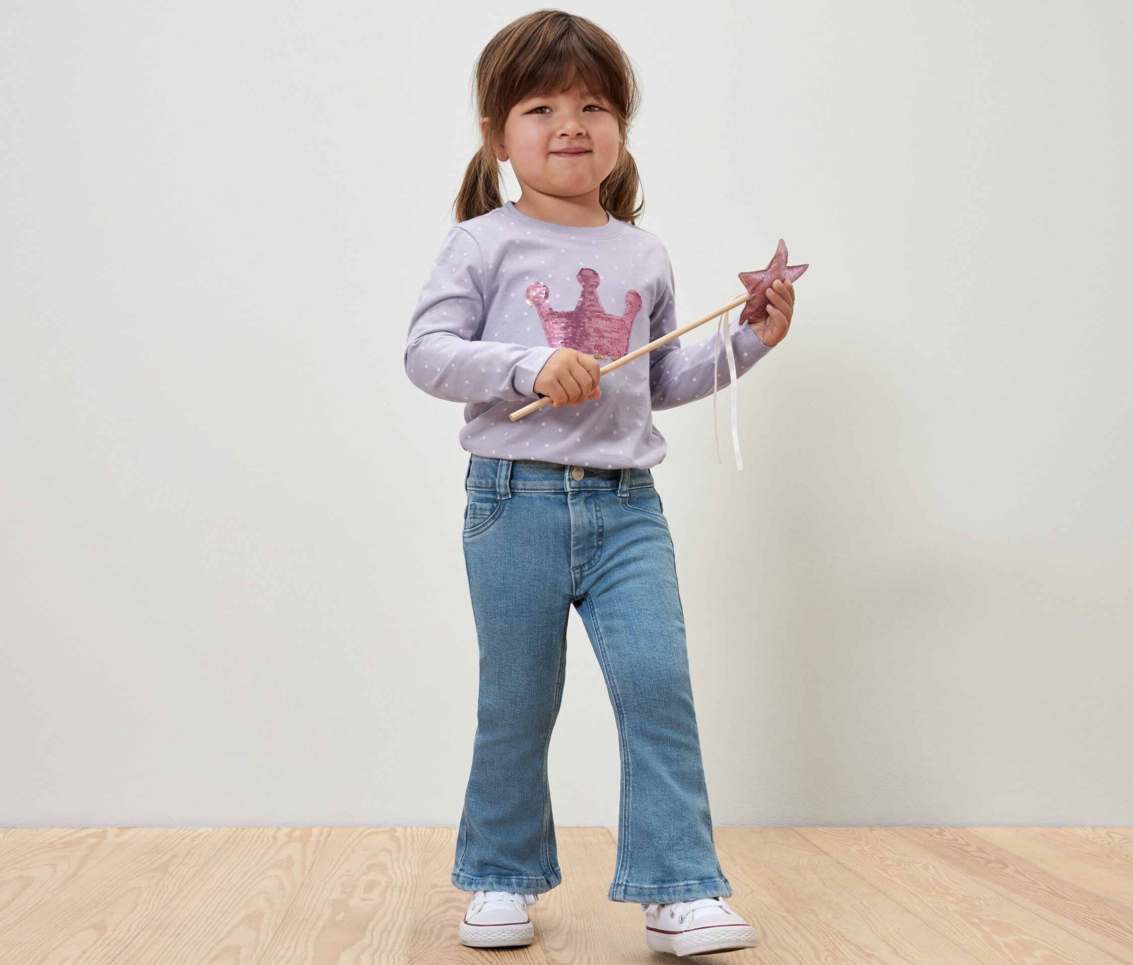Fillette souriante tenant une baguette étoilée et portant un Jeans pour enfant ‒ Fit « Emma ».