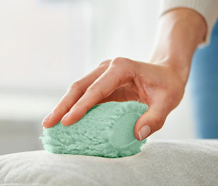 Une femme nettoie un coussin avec 2 éponges antitaches.