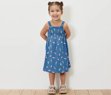 Une petite fille souriante pose dans une robe à bretelles bleu clair avec un motif de glace.