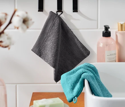 Un gant de toilette gris est accroché à un crochet et un gant de toilette turquoise repose sur un lavabo. Il y a aussi du savon.