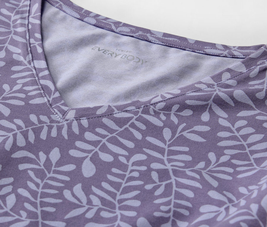 Détail d'un t-shirt violet avec un imprimé de feuilles et un col en V.