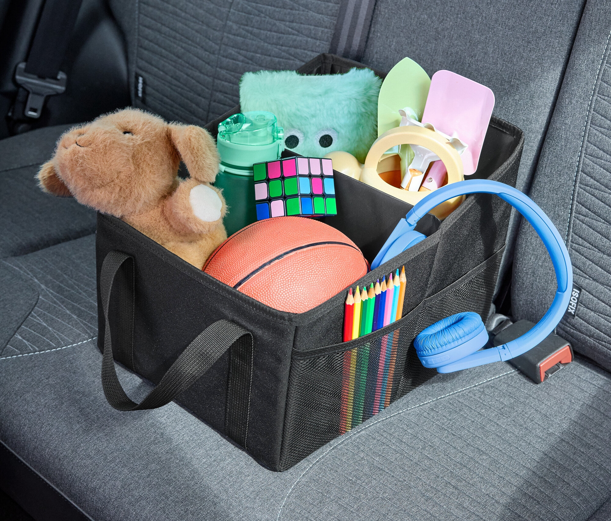 Dans un sac noir dans la voiture, il y a des jouets, des crayons de couleur, des écouteurs et d'autres objets.