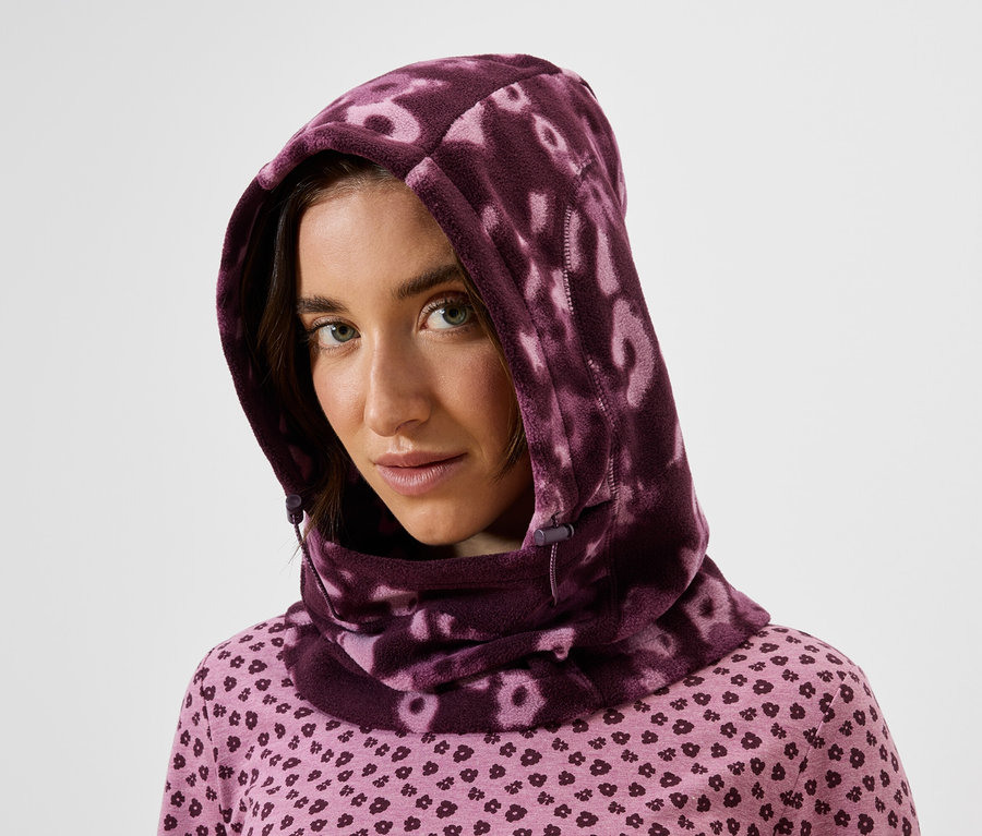 Portrait d'une femme aux cheveux bruns portant un haut rose à motifs et une cagoule écharpe violette.