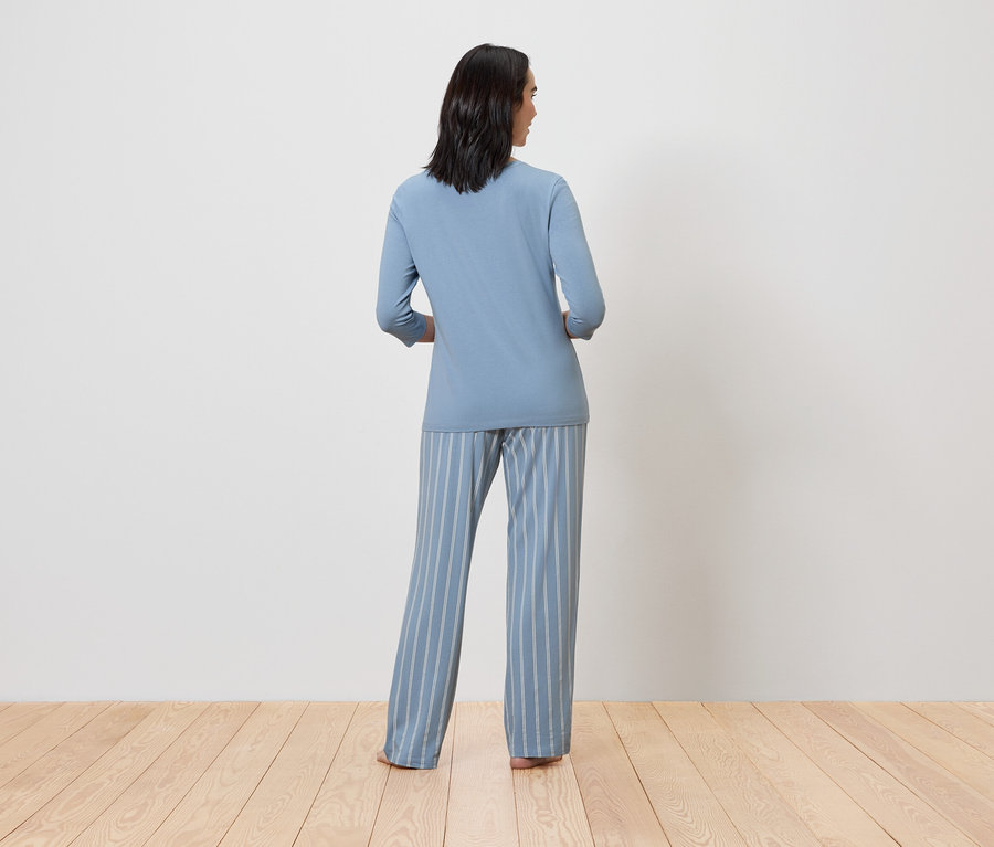 Une femme en pyjama bleu avec un pantalon rayé, vue de dos.