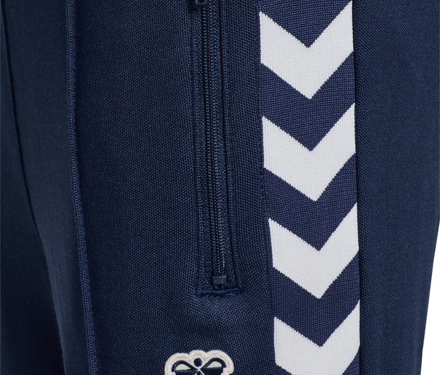 Gros plan sur un pantalon bleu marine HUMMEL HMLJR Archive Regular Poly Pants avec fermeture éclair et logo blanc.