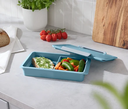 Pain, tomates, basilic et une boîte à collation bleue avec un couvercle ouvert sur un comptoir.