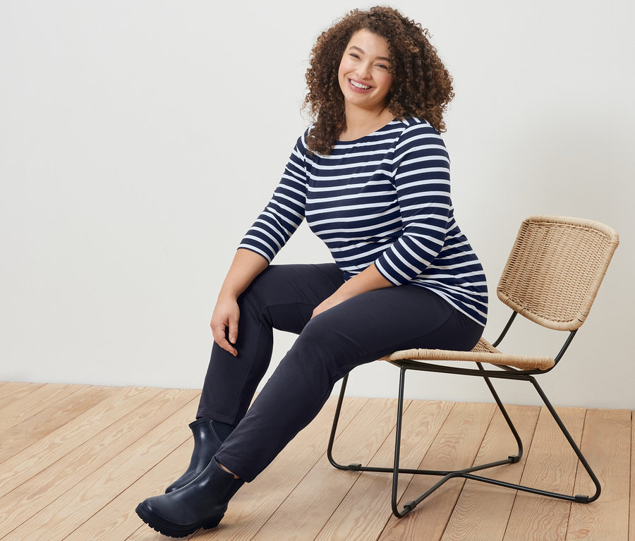 Une femme assise sur une chaise porte un t-shirt rayé manches 3/4 et un pantalon de jogging bleu marine.