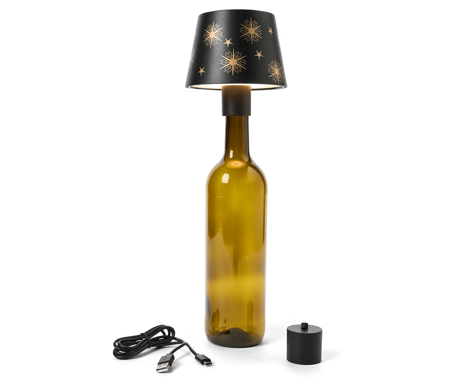 Lampe de table faite d'une bouteille en verre vert olive avec un abat-jour noir orné d'étoiles dorées. Un câble USB et un interrupteur noir sont posés à côté de la lampe.