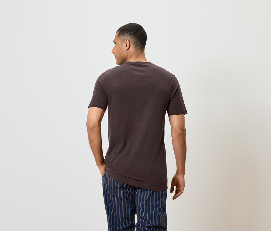 Un homme vu de dos porte un t-shirt marron et un pantalon rayé bleu.