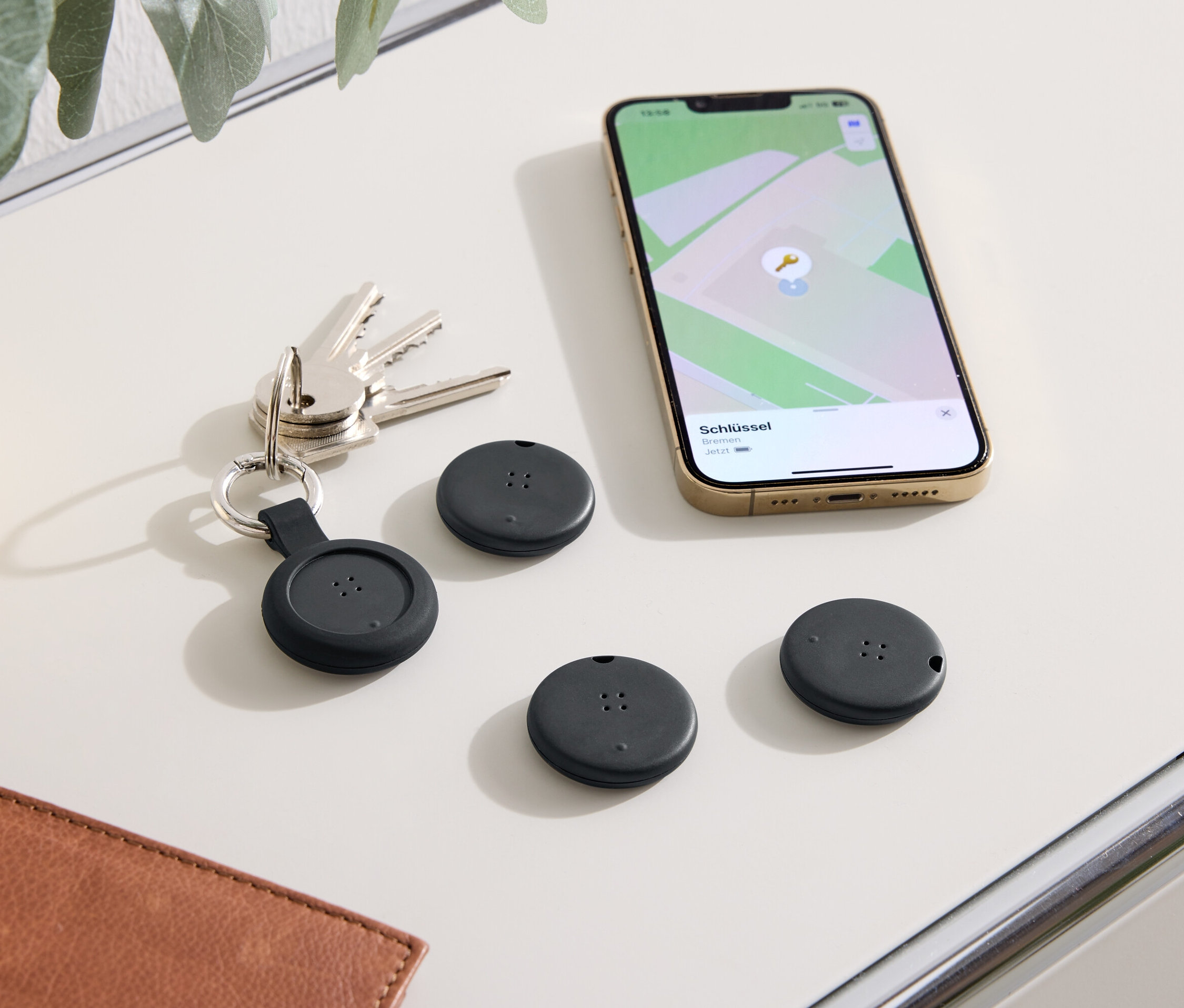 Sur une table sont disposés des clés, un téléphone affichant une carte et trois localisateurs noirs.