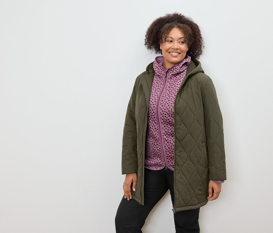 Femme portant un manteau matelassé olive et un sweat à capuche à motifs violets.