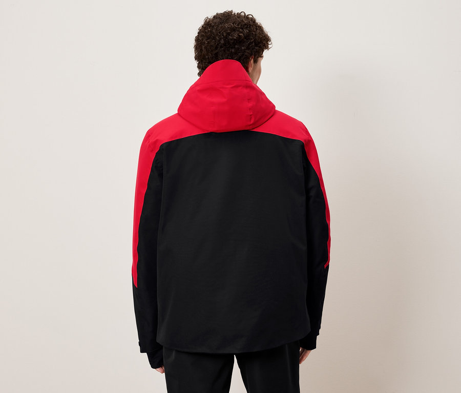 Un homme vu de dos porte une veste à capuche noire et rouge.