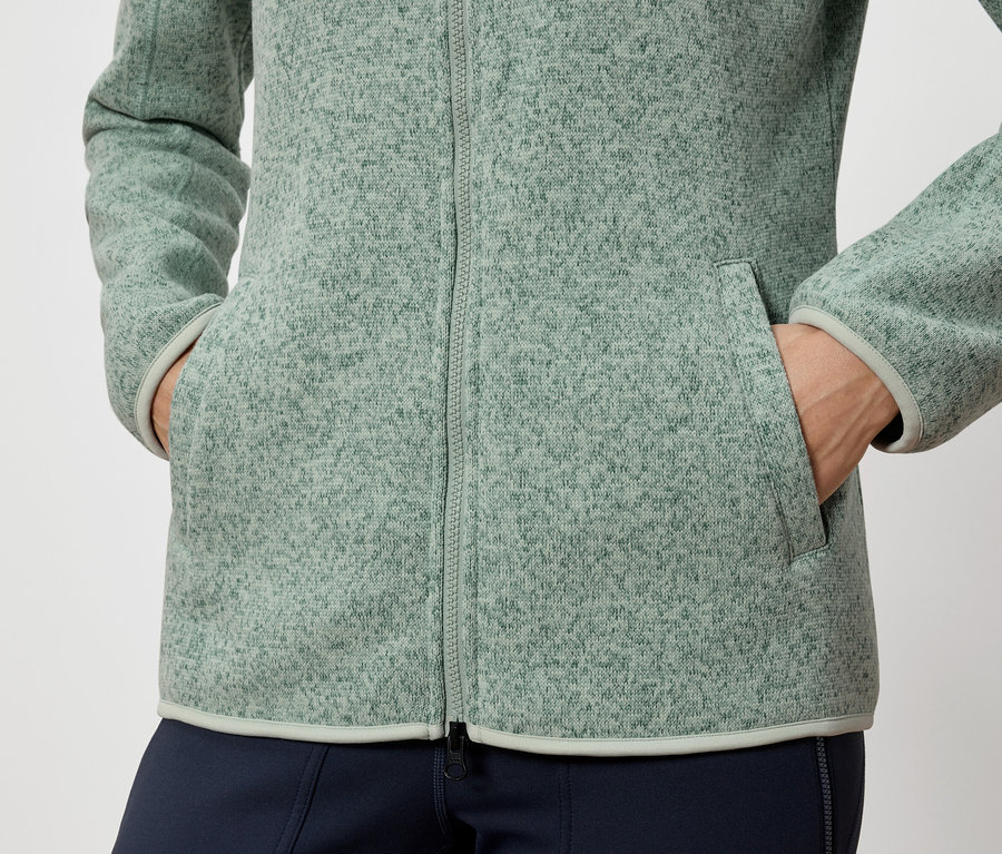 Une personne a les mains dans les poches d'une veste polaire verte.