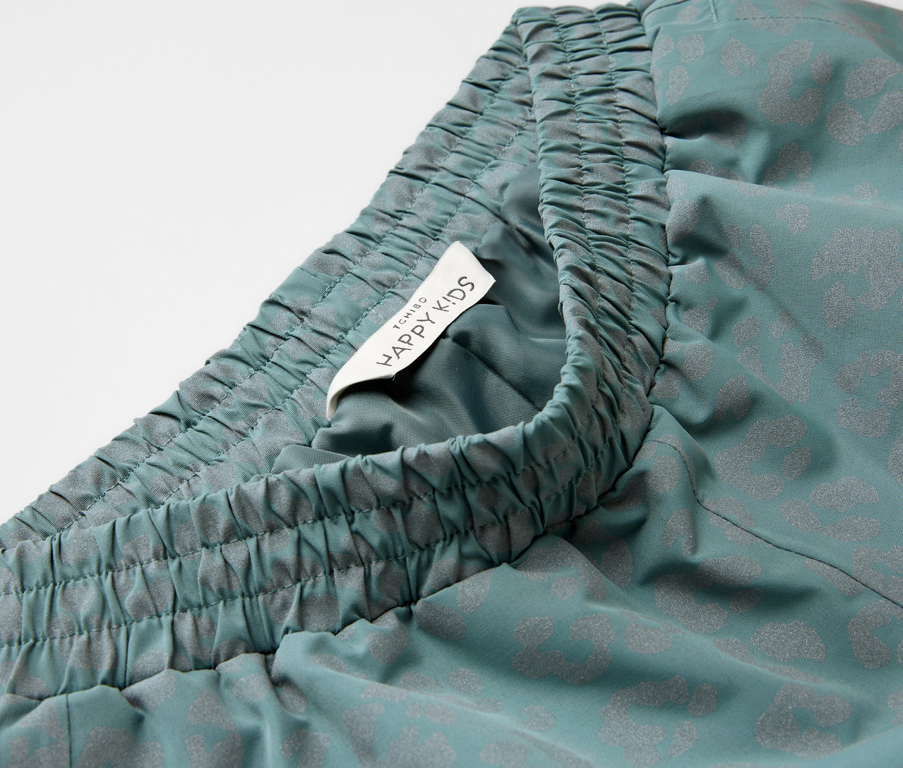 Gros plan sur un pantalon de pluie pour enfant avec des éléments réfléchissants, une taille élastique et une étiquette Happy Kids.