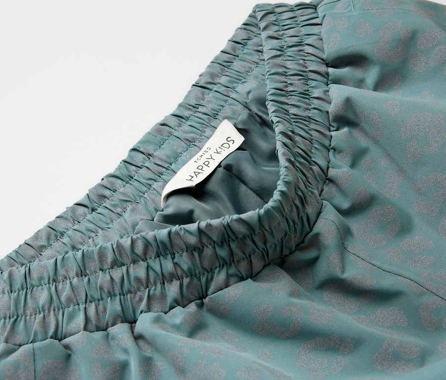 Gros plan sur un pantalon de pluie pour enfant avec des éléments réfléchissants, une taille élastique et une étiquette Happy Kids.