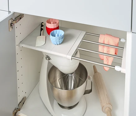 Dans une armoire de cuisine, il y a une étagère flexible, un robot de cuisine, un rouleau à pâtisserie et des moules en silicone.