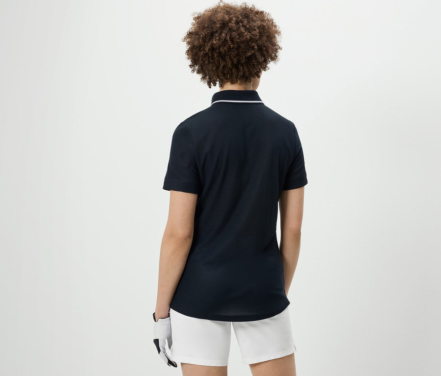 Vue arrière d'une femme aux cheveux bouclés portant un polo technique bleu foncé et un short blanc.