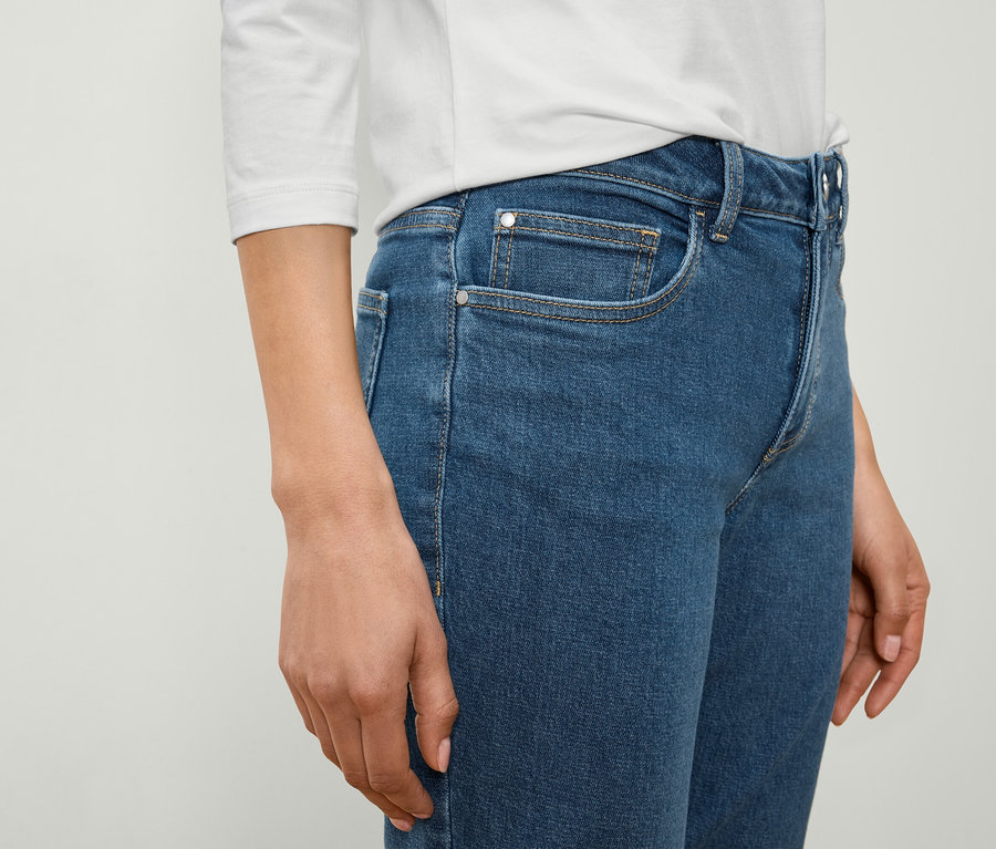 Une femme porte un jean bleu et une chemise blanche.