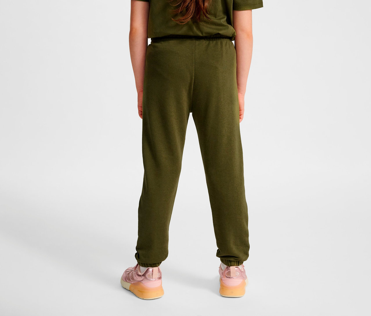 Vue arrière d'un enfant portant un pantalon régulier HUMMEL HMLJR Base vert et des chaussures roses.