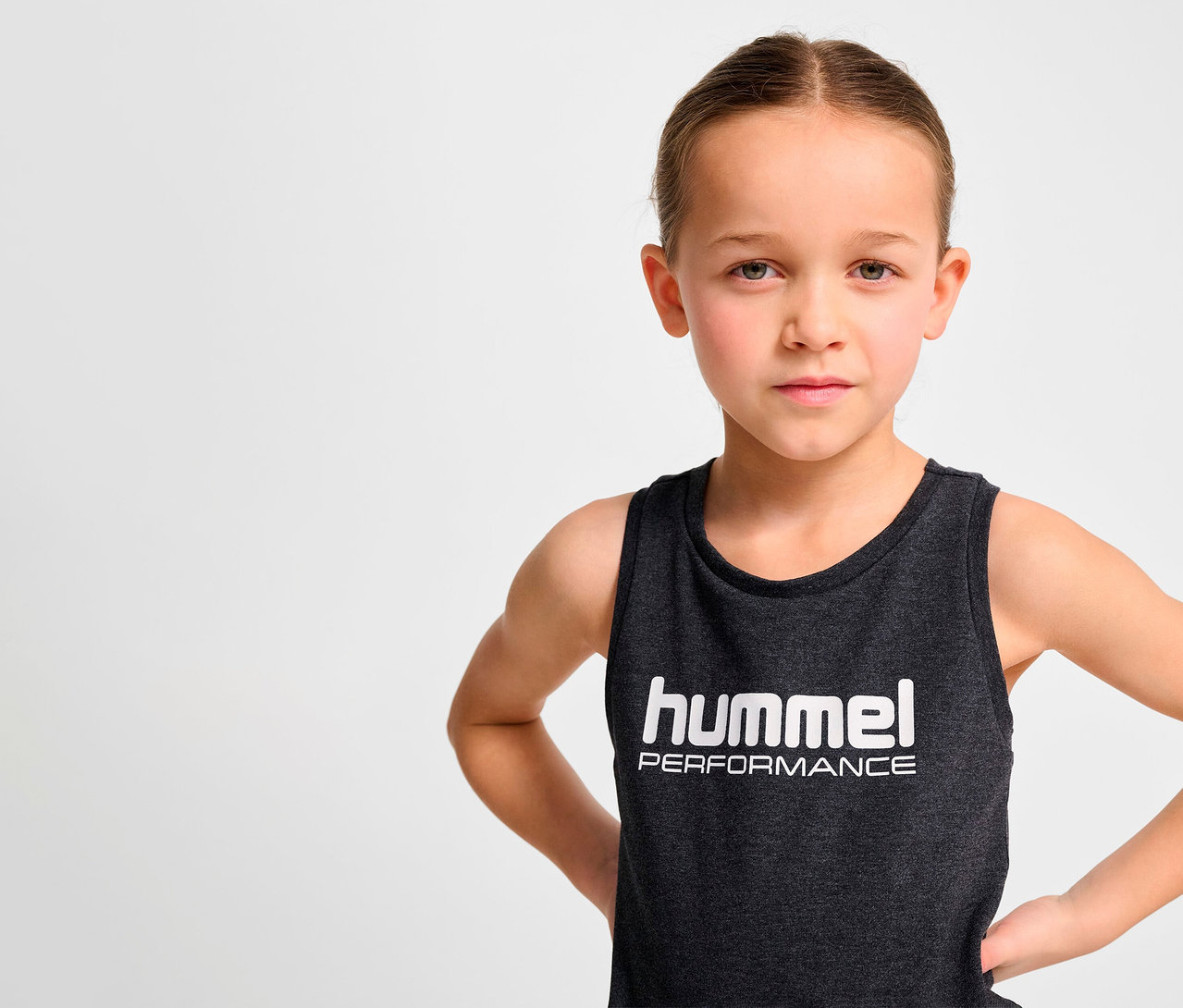 Portrait d'une fille les mains sur les hanches portant un top HUMMEL HMLJR noir.
