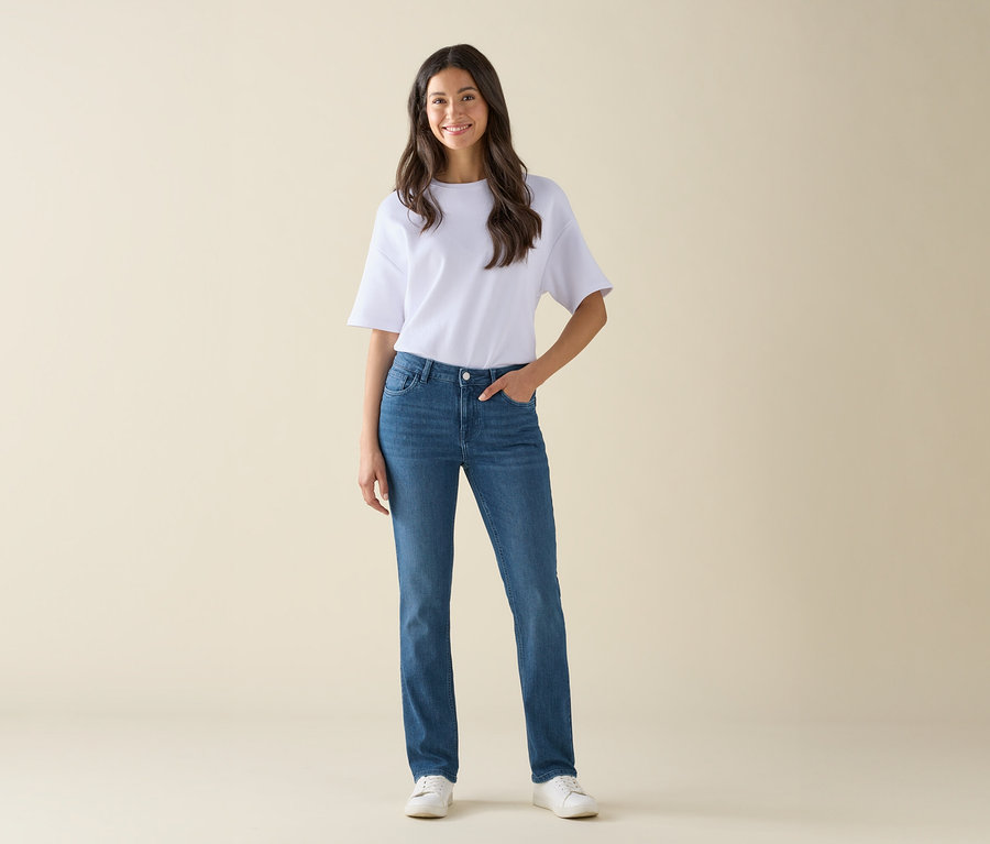 Une femme se tient debout et pose en jean bleu, t-shirt blanc et chaussures blanches.