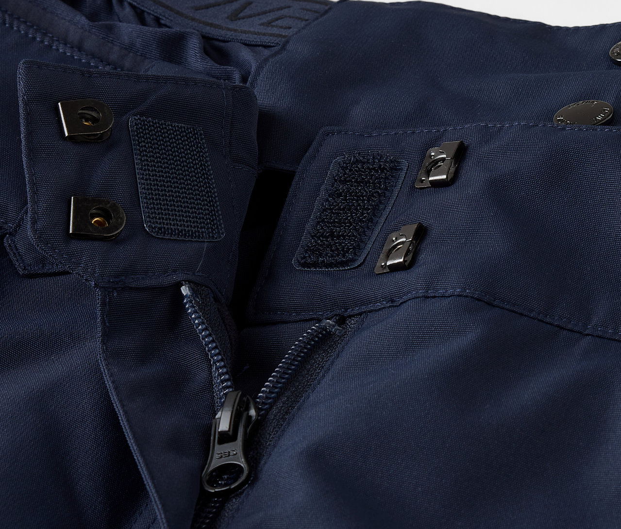 Gros plan sur une veste bleu marine avec fermeture éclair, velcro et boutons.
