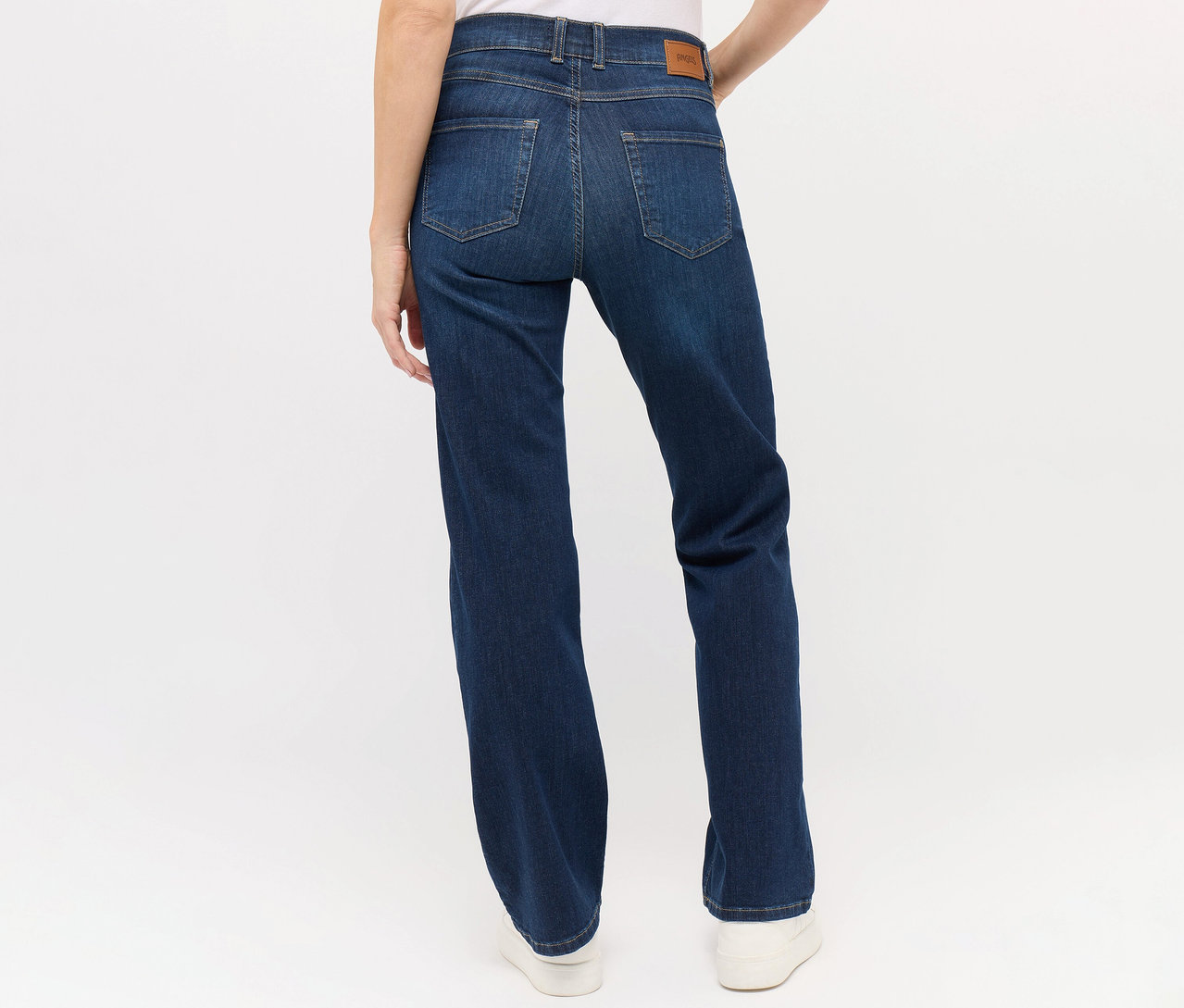 Vue arrière d'une femme portant un jean Angels « Lara » coupe droite bleu foncé et des chaussures blanches.