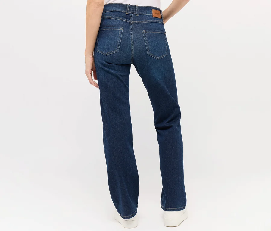 Vue arrière d'une femme portant un jean Angels « Lara » coupe droite bleu foncé et des chaussures blanches.