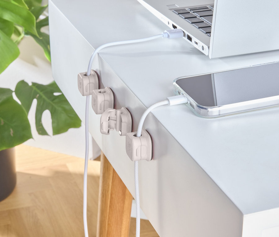 Un ordinateur portable argenté et un téléphone sont en charge sur un bureau blanc avec des supports de câbles en bois.