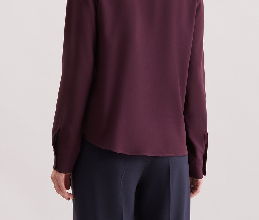 De dos, une femme aux cheveux blonds porte une chemise à manches longues violette.