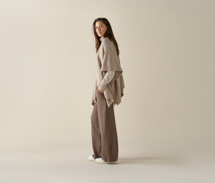 Une femme pose en pantalon marron et cardigan beige avec des baskets blanches Tom Tailor en PU.