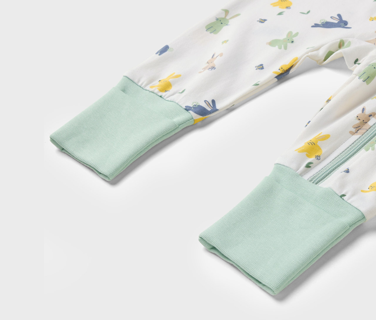 Gros plan sur un pyjama une-pièce pour enfant avec un motif de lapins et des poignets vert clair.