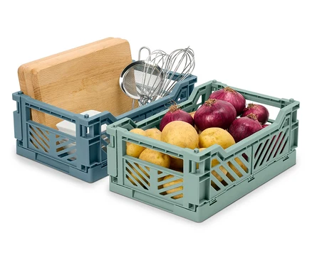 Deux caisses pliantes : une bleue avec une planche à découper et des ustensiles de cuisine, une verte avec des pommes de terre et des oignons.