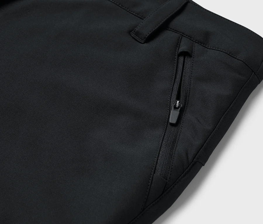 Détail d'un pantalon noir avec une poche zippée.