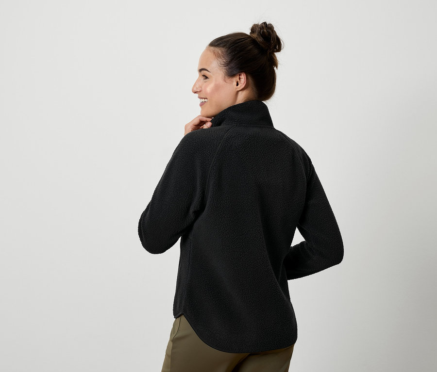 Une femme regardant par-dessus son épaule porte un haut en polaire noir et un pantalon kaki.