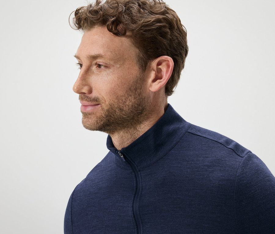 Portrait d'un homme aux cheveux bruns ondulés et à la barbe, portant un pull bleu zippé.