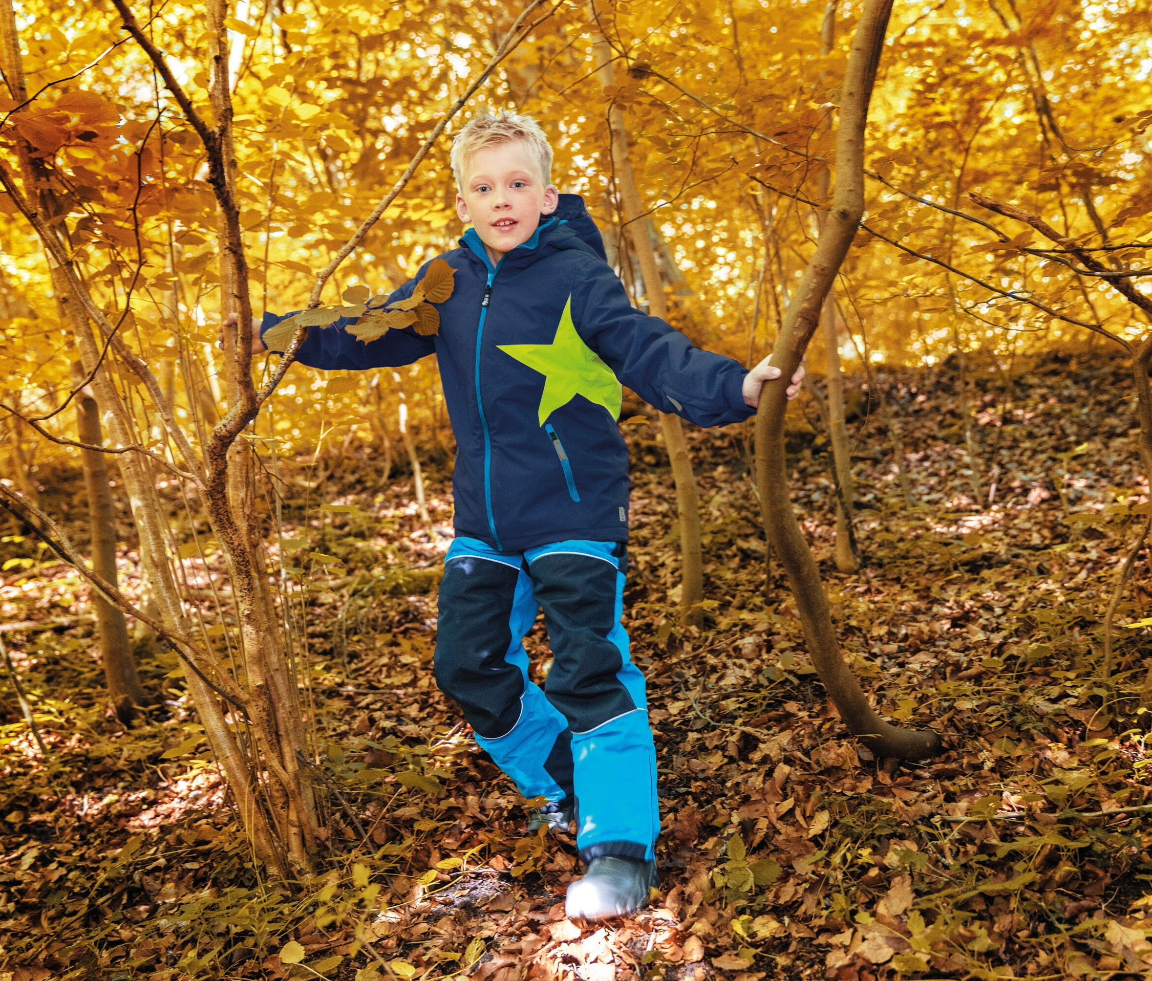 Un garçon en vêtements bleu et noir avec une étoile marche dans une forêt d'automne.