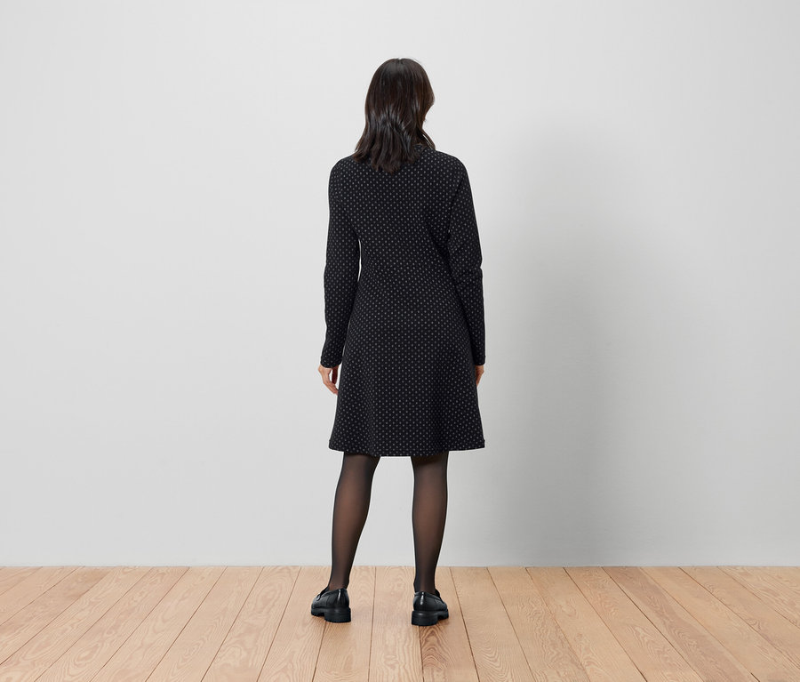 Une femme se tient dos à la caméra et porte une robe noire et des collants.