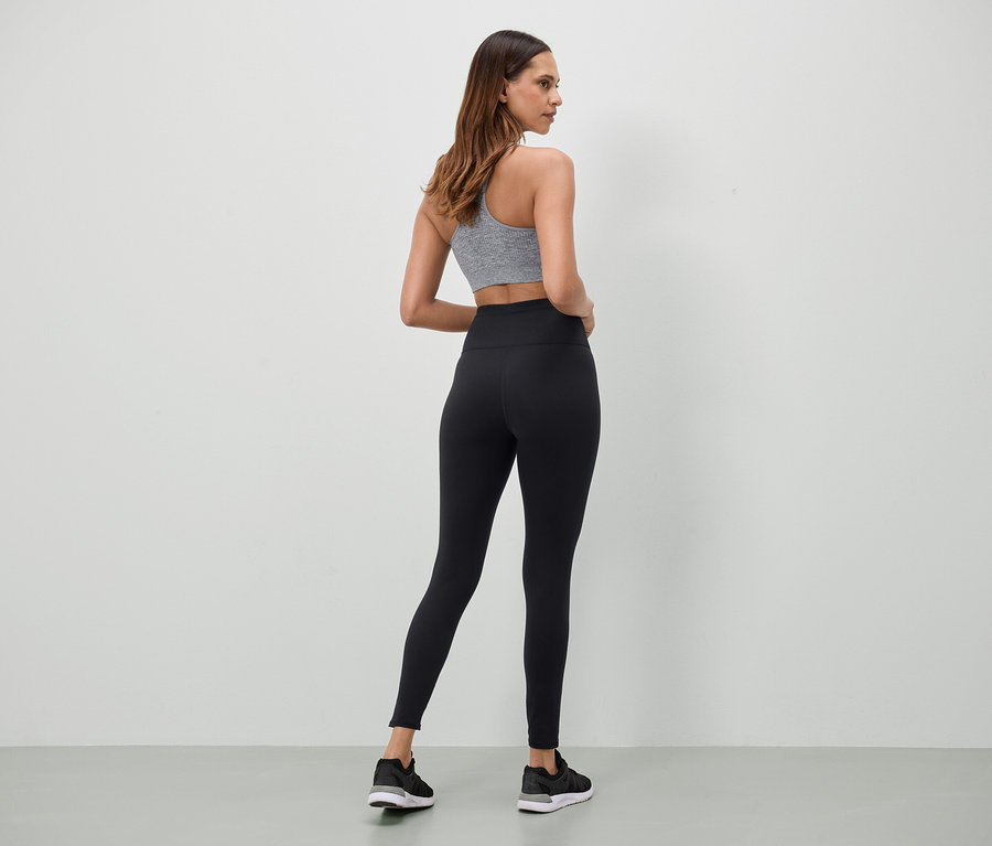 Une femme portant un soutien-gorge de sport gris et un legging noir se tient dos à l'appareil photo.