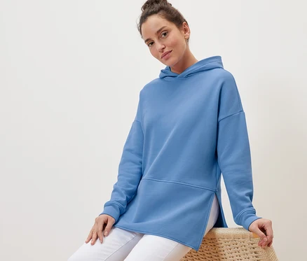 Femme assise sur un fauteuil en osier portant un sweatshirt long à capuche bleu clair.