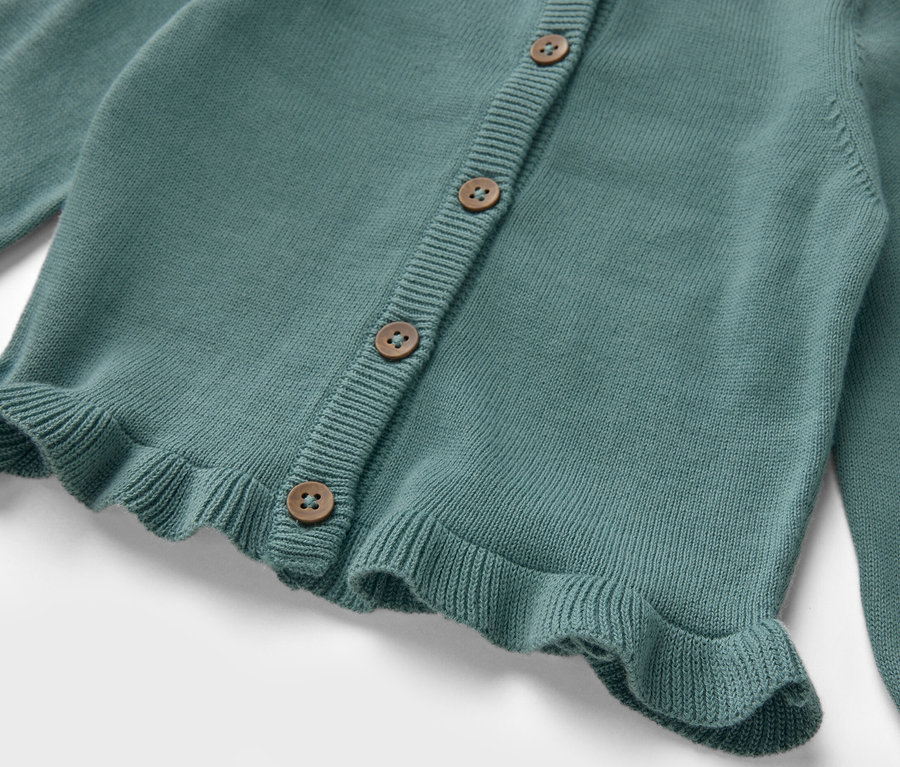 Gros plan sur une veste en maille pour enfant avec des boutons et des volants.